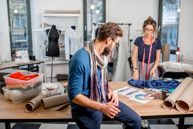 Alguns designers de moda trabalhando com esboços de tecidos e roupas em um estúdio cheio de ferramentas e equipamentos de alfaiataria