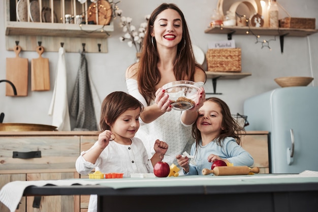 Alguns doces não interferem. Jovem mulher bonita dar os biscoitos enquanto eles sentados perto da mesa com brinquedos