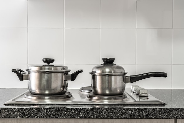 Alguns potes de inox no fogão de cozinha com bancada de mármore e parede de azulejos brancos