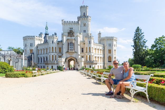 Alguns turistas estão sentados em um banco em frente ao belo castelo Hluboka nad Vltavou - República Tcheca.