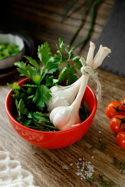 Alho e salsa em um prato sobre um fundo de madeira com tomate cereja e sal