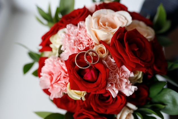 Alianças de casamento em um buquê de rosas vermelhas e brancas.