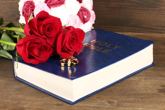 Alianças de casamento na Bíblia com rosas em fundo de madeira