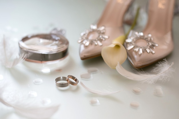 Alianzas de oro con plumas junto a los zapatos beis de la novia decorados con piedras sobre las que reposa una flor amarilla y junto a un frasco de perfume Chanel