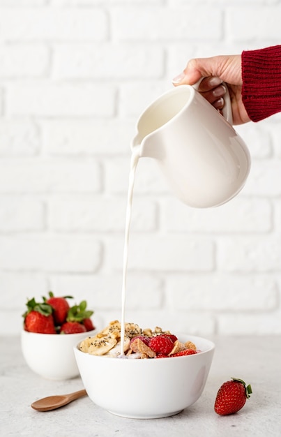 Alimentação e dieta saudáveis. mão feminina servindo leite na tigela de cereal do café da manhã no fundo da parede de tijolo branco