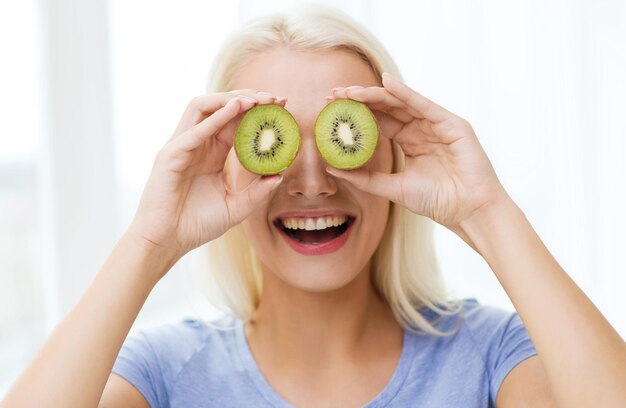 alimentação saudável, alimentos orgânicos, dieta de frutas, conceito de quadrinhos e pessoas - mulher feliz se divertindo e cobrindo os olhos com kiwi