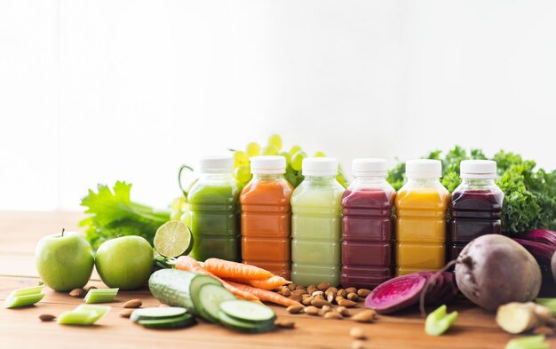 alimentação saudável, bebidas, dieta e conceito de desintoxicação - garrafas de plástico com diferentes sucos de frutas ou vegetais e alimentos na mesa de madeira