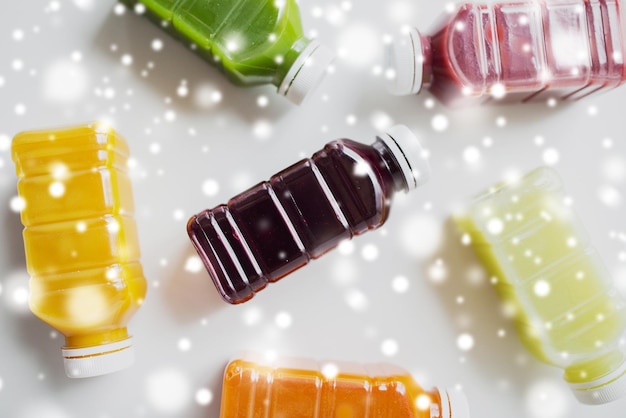 Foto alimentação saudável, bebidas, dieta e conceito de desintoxicação - garrafas de plástico com diferentes sucos de frutas ou vegetais em branco sobre neve