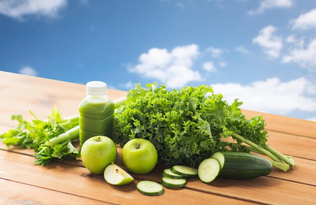 alimentação saudável, comida, dieta e conceito vegetariano - garrafa com suco verde, frutas e legumes na mesa de madeira sobre fundo de céu azul