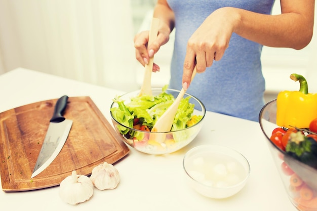 alimentação saudável, comida vegetariana, dieta e conceito de pessoas - close-up de jovem cozinhar salada de legumes em casa