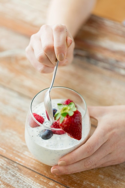 Foto alimentação saudável, comida vegetariana, dieta e conceito de pessoas - close-up de mãos de mulher com iogurte e frutas na mesa
