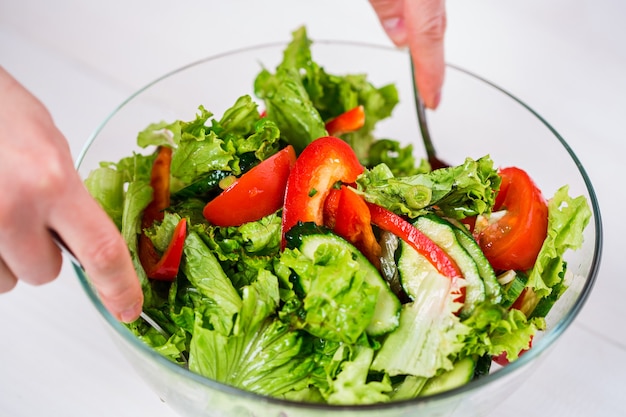 Alimentação saudável, comida vegetariana, dieta e conceito de pessoas - close-up de uma jovem mulher temperando salada de vegetais com azeite de oliva em um fundo branco