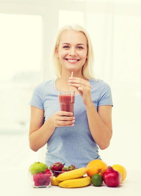 alimentação saudável, comida vegetariana, dieta e conceito de pessoas - mulher sorridente bebendo suco de frutas de vidro em casa