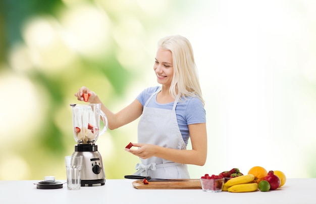 alimentação saudável, culinária, comida vegetariana, dieta e conceito de pessoas - jovem sorridente colocando frutas e bagas para shake de frutas para liquidificador sobre fundo verde natural