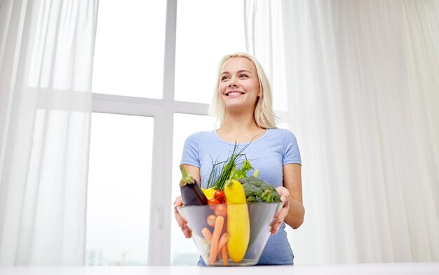 alimentação saudável, culinária, comida vegetariana, dieta e conceito de pessoas - jovem sorridente com tigela de legumes em casa