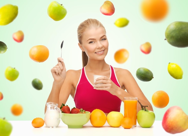 alimentação saudável, dieta, alimentos orgânicos e conceito de pessoas - mulher feliz comendo iogurte e tomando café da manhã sobre fundo verde com frutas caindo