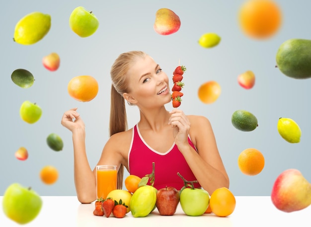 alimentação saudável, dieta, desintoxicação, alimentos orgânicos e conceito de pessoas - jovem feliz com suco e frutas comendo morangos sobre fundo cinza