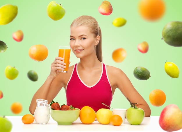 alimentação saudável, dieta, desintoxicação e conceito de pessoas - jovem feliz tomando café da manhã e bebendo suco de laranja sobre fundo verde com frutas caindo