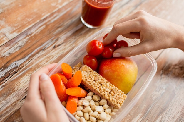 alimentação saudável, dieta e conceito de pessoas - close-up de mãos de mulher com comida em recipiente plástico e suco de tomate fresco na cozinha de casa