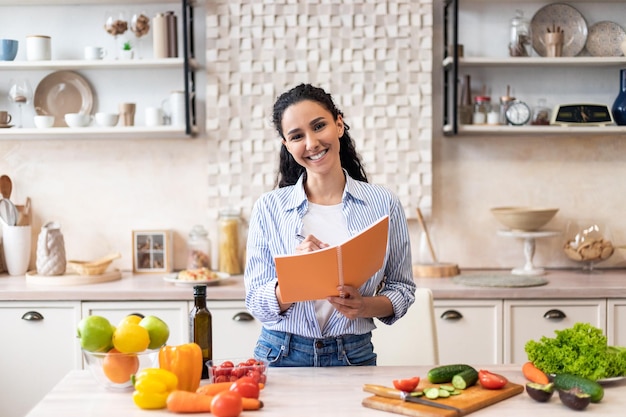 Alimentação saudável e conceito de dieta mulher excitada fazendo lista de alimentos necessários na cozinha segurando