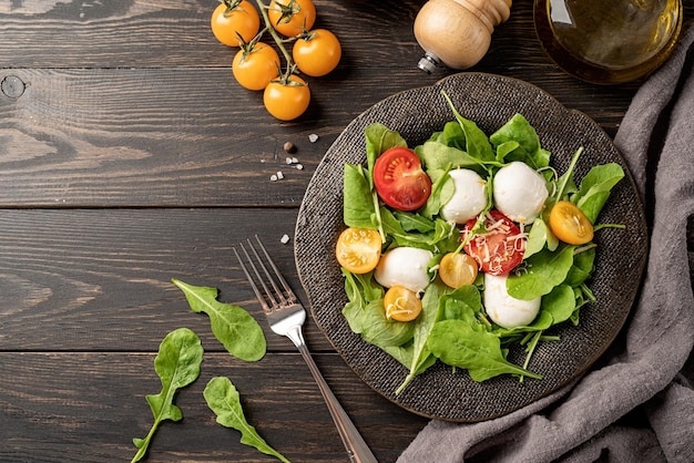 Alimentação saudável e dieta Salada fresca com queijo mussarela de tomate cereja rúcula e queijo duro em fundo escuro de madeira Vista superior