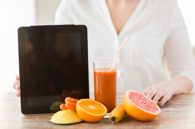 alimentação saudável, tecnologia, dieta e conceito de pessoas - close-up de mãos de mulher com tablet pc, frutas e suco fresco sentado à mesa