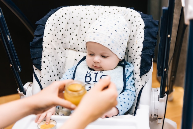 Alimentación. Adorable bebé niño comiendo con una cuchara en silla alta. Bebé