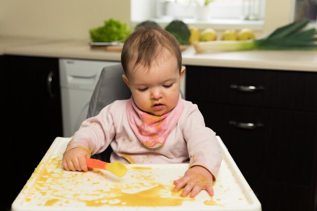 Alimentación. Adorable bebé niño comiendo con una cuchara en una silla para niños.