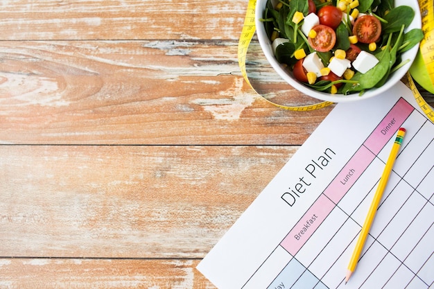 Foto alimentación saludable, alimentos, adelgazamiento y concepto de pérdida de peso - primer plano de papel de plan de dieta con cinta métrica y ensalada