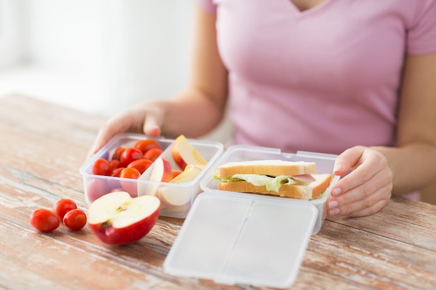 alimentación saludable, almacenamiento, dieta y concepto de personas: cierre de una mujer con comida en un recipiente de plástico en la cocina de casa