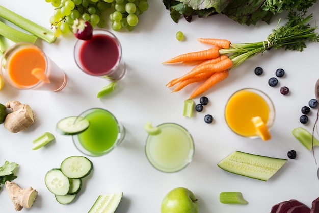 Foto alimentación saludable, bebidas, dieta y concepto de desintoxicación: cierre de vasos con diferentes jugos de frutas o vegetales y comida en la mesa