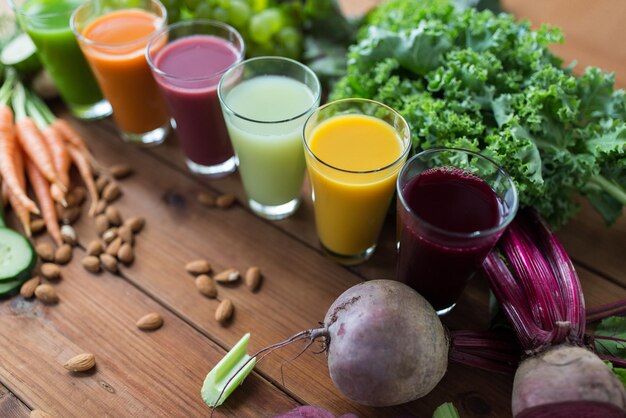 alimentación saludable, bebidas, dieta y concepto de desintoxicación - vasos con diferentes jugos de frutas o vegetales y comida en la mesa