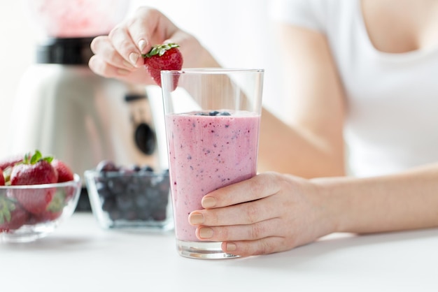 alimentación saludable, cocina, comida vegetariana, dieta y concepto de personas - cierre de manos de mujer decorando batido con fresa en casa