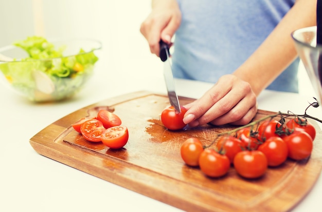 alimentación saludable, cocina, comida vegetariana, dieta y concepto de personas - cierre de mujer cortando tomates con cuchillo en tabla de cortar