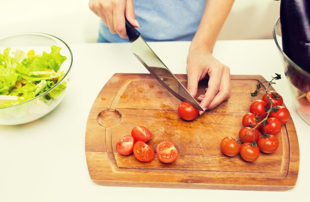 alimentación saludable, cocina, comida vegetariana, dieta y concepto de personas - cierre de mujer cortando tomates con cuchillo en tabla de cortar