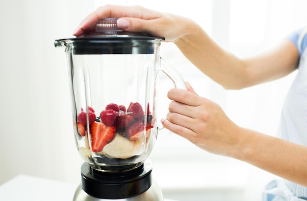 Foto alimentación saludable, cocina, comida vegetariana, dieta y concepto de personas: cierre de una mujer con licuadora haciendo batido de frutas en casa