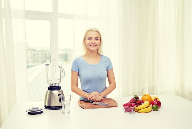 alimentación saludable, cocina, comida vegetariana, dieta y concepto de personas - mujer joven sonriente con licuadora y frutas en casa