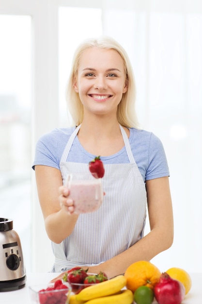alimentación saludable, cocina, comida vegetariana, dieta y concepto de personas - mujer sonriente sosteniendo un vaso de batido de frutas en casa