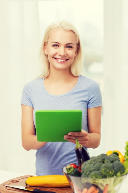 alimentación saludable, cocina, comida vegetariana, tecnología y concepto de personas - mujer joven sonriente con computadora de tablet pc y tazón de verduras en casa