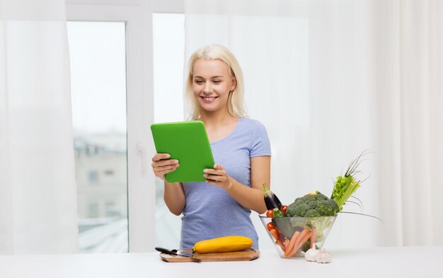 alimentación saludable, cocina, comida vegetariana, tecnología y concepto de personas - mujer joven sonriente con computadora de tablet pc y tazón de verduras en casa