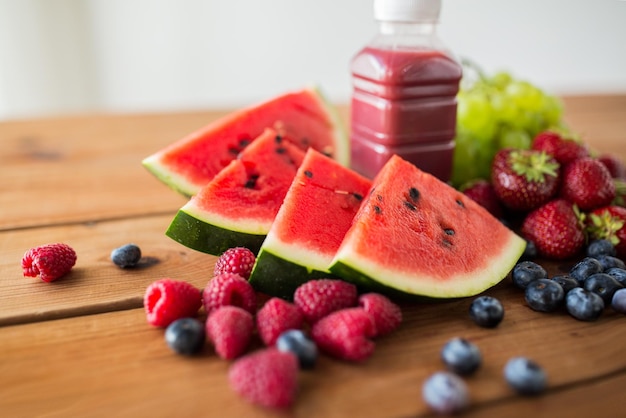 alimentación saludable, comida, dieta y concepto vegetariano - botella con jugo de frutas y bayas o batido en una mesa de madera