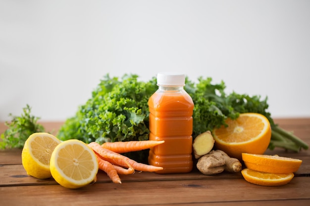 alimentación saludable, comida, dieta y concepto vegetariano - botella con jugo de zanahoria, frutas y verduras en la mesa de madera