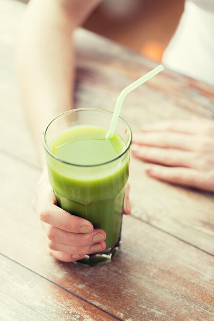 alimentación saludable, comida, dieta, desintoxicación y concepto de personas: cierre de manos de mujer con jugo verde en una mesa de madera