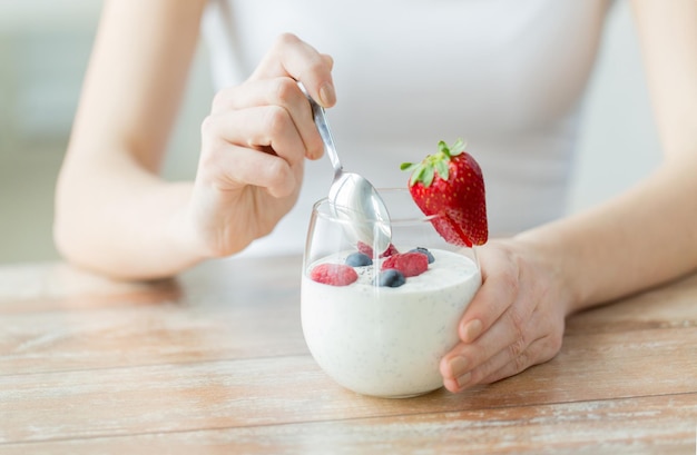 Foto alimentación saludable, comida vegetariana, dieta y concepto de personas - cierre de manos de mujer con yogur y bayas en la mesa