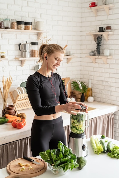 Alimentación saludable, concepto de dieta. Joven mujer sonriente rubia haciendo batido verde en la cocina de casa