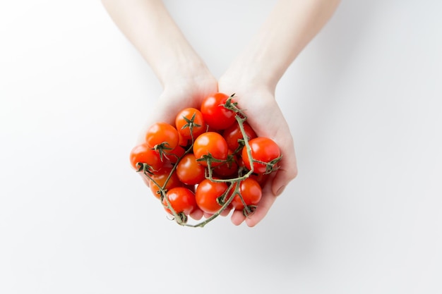 alimentación saludable, dieta, comida vegetariana y concepto de personas - cierre de manos de mujer sosteniendo un montón de tomates de cerezo en casa