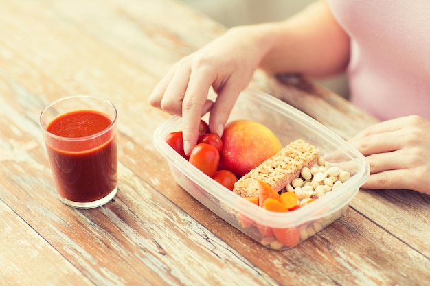 alimentación saludable, dieta y concepto de personas - cierre de manos de mujer con comida en recipiente de plástico y jugo de tomate fresco en la cocina de casa