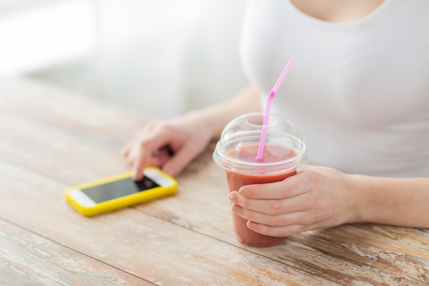 alimentación saludable, dieta, tecnología y concepto de personas - cierre de mujer con smartphone y taza de batido sentado en la mesa