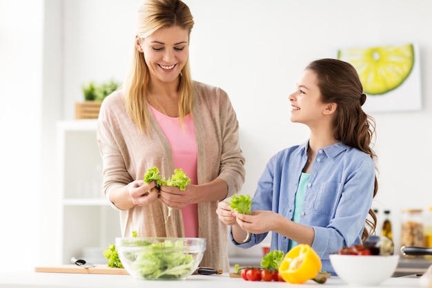alimentación saludable, familia y concepto de personas - madre y hija felices cocinando ensalada de verduras para la cena en la cocina de casa