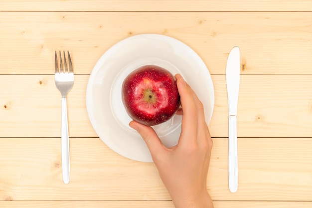 Alimentación saludable La mano de una mujer pone una manzana roja madura en una vista superior de un plato blanco